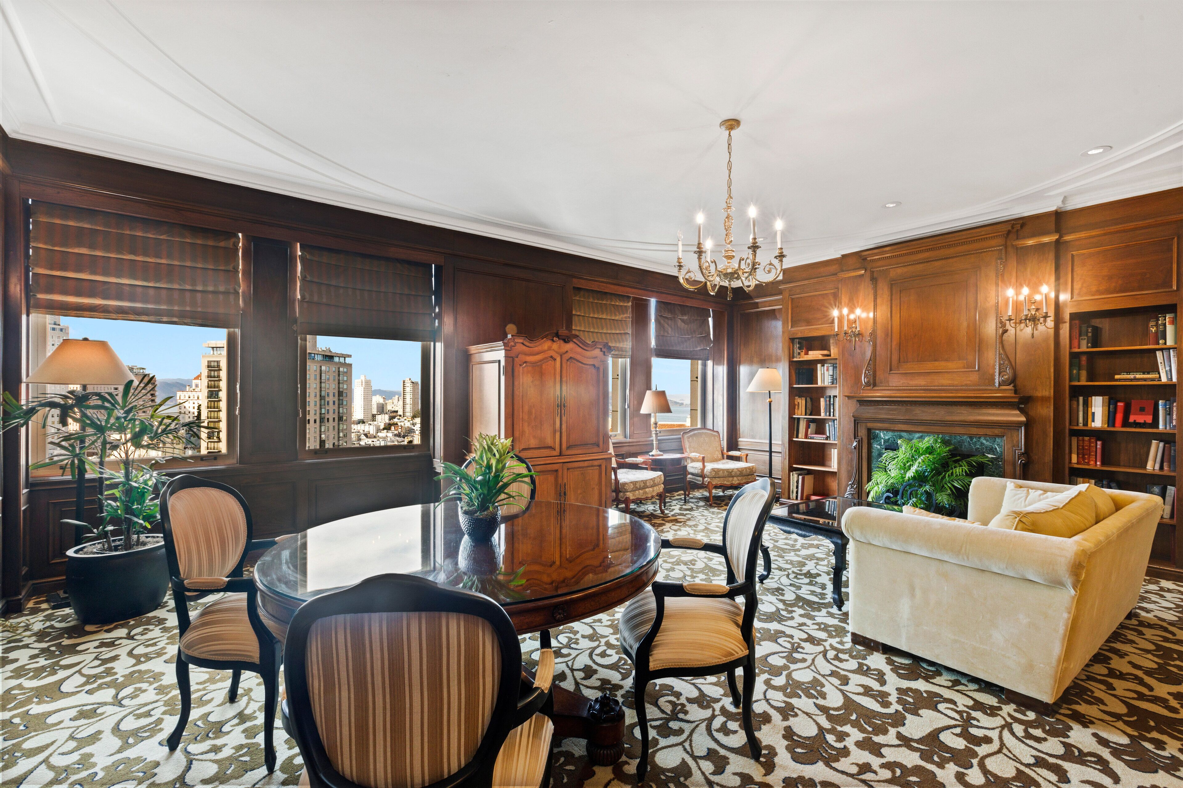 A spacious living room with a round table, comfortable seating, a fireplace, and a bookshelf.