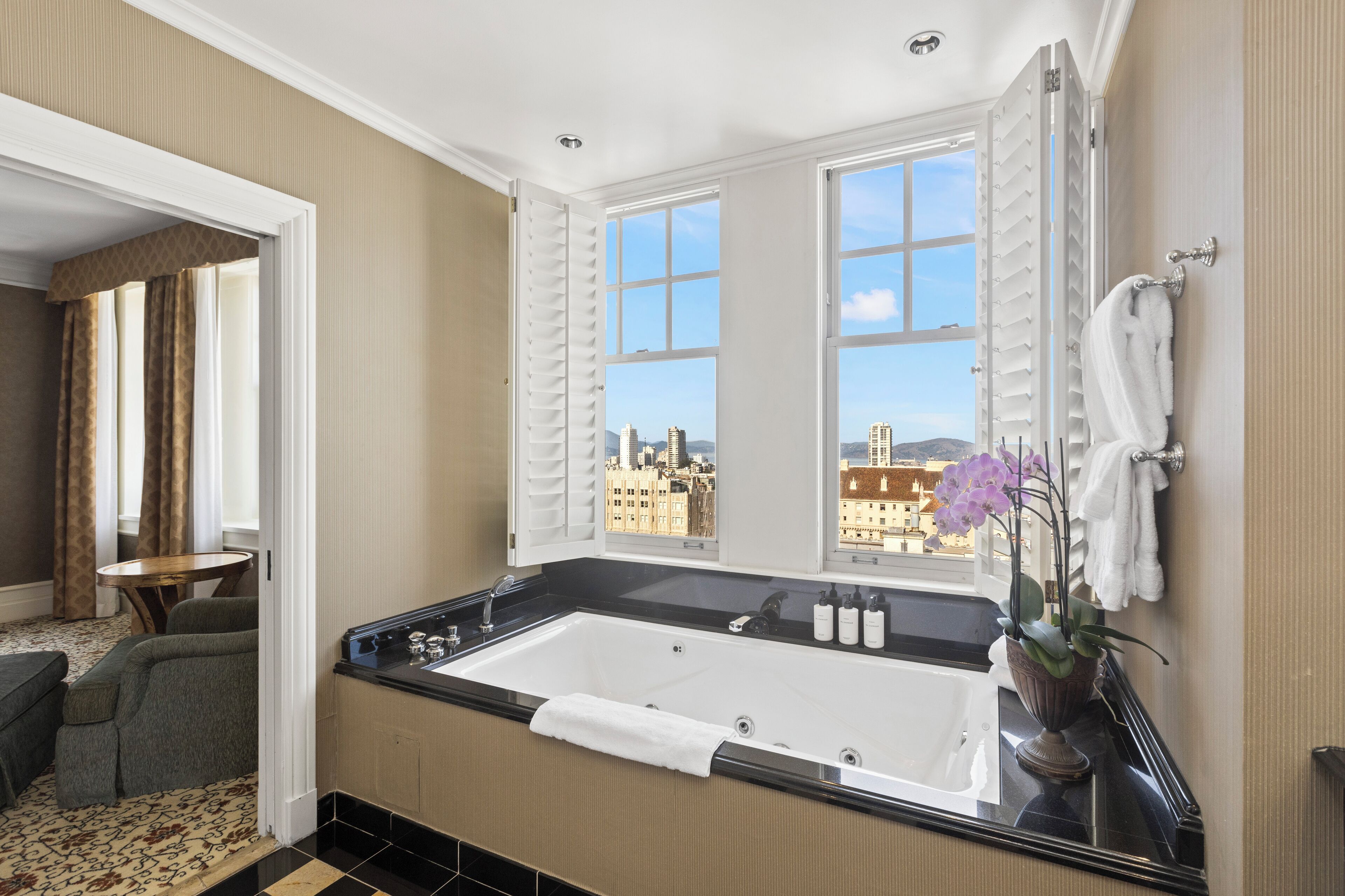 Un baño moderno con una bañera grande, vistas de la ciudad a través de amplios ventanales y un pequeño rincón de descanso con una mesa.