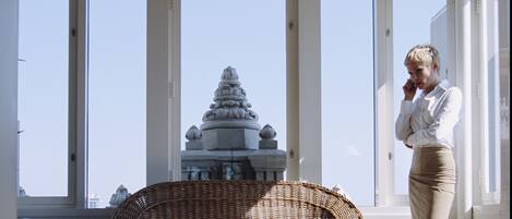 A room with large windows, wicker furniture, and a view of a temple.
