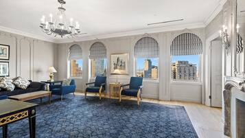 A spacious room with a patterned carpet, a chandelier, a fireplace, and a view of the city through large windows.