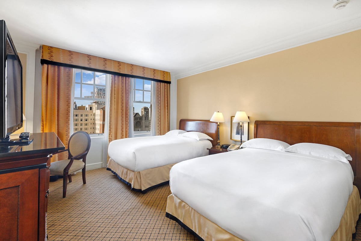 A hotel room with two beds, a desk, a chair, a TV, and a window with curtains.