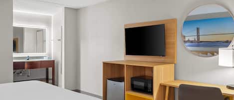 A hotel room with a bed, a desk with a computer, a microwave, and a TV on the wall.