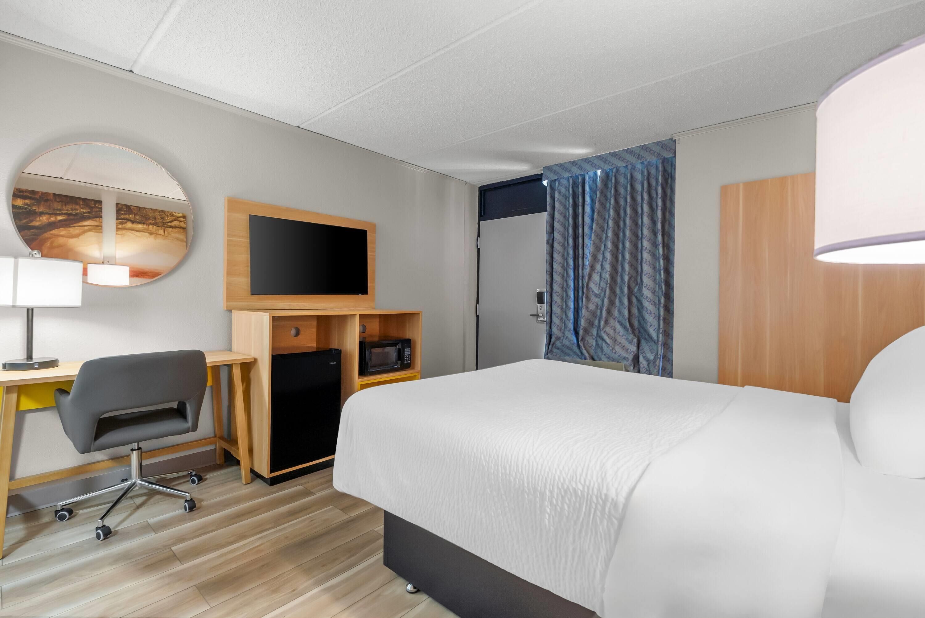 A hotel room with a bed, a desk with a chair, a television, a microwave, and a wardrobe.