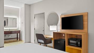 A hotel room with a bed, a desk, a chair, a TV, a microwave, and a bathroom visible through an open door.