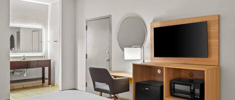 A hotel room with a bed, a desk, a chair, a TV, a microwave, and a bathroom visible through an open door.