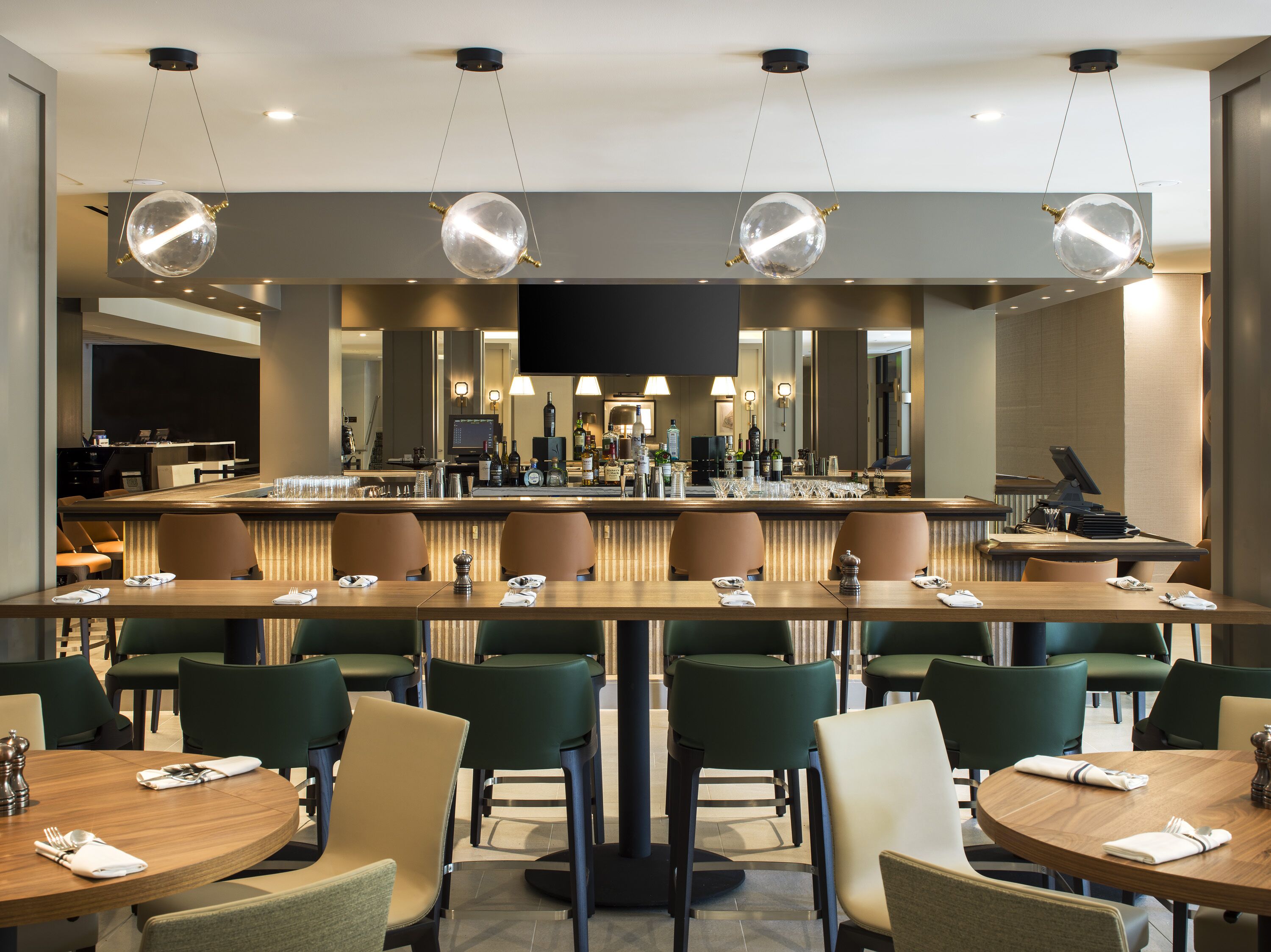 Eine moderne Hotelbar mit verschiedenen Sitzbereichen, einer Bar und einem großen Flachbildfernseher.