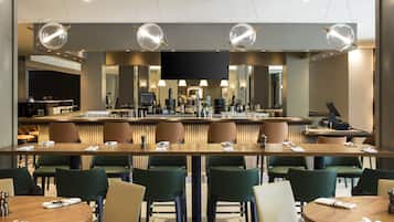 Eine moderne Hotelbar mit verschiedenen Sitzbereichen, einer Bar und einem großen Flachbildfernseher.