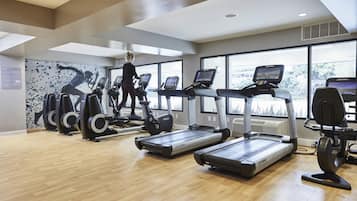Een sportschool met loopbanden, elliptische trainers en een groot raam dat voor natuurlijk licht zorgt.
