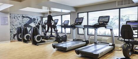 A gym with treadmills, elliptical machines, and a large window providing natural light.