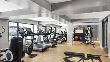 A modern gym with treadmills, elliptical machines, and a bench press area.