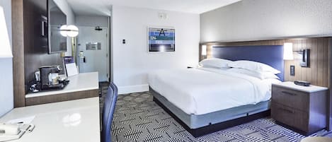 A hotel room with a large bed, a desk with a chair, a desk lamp, and a wall-mounted TV.