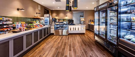 A modern cafe interior with a wooden floor, a counter with snacks and beverages, and a refrigerated drinks display.