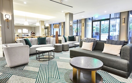 A modern hotel lobby with a seating area, a bar, and large windows.