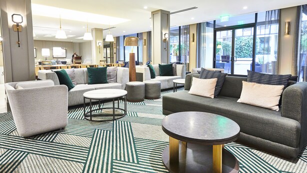 A modern hotel lobby with a seating area, a bar, and large windows.