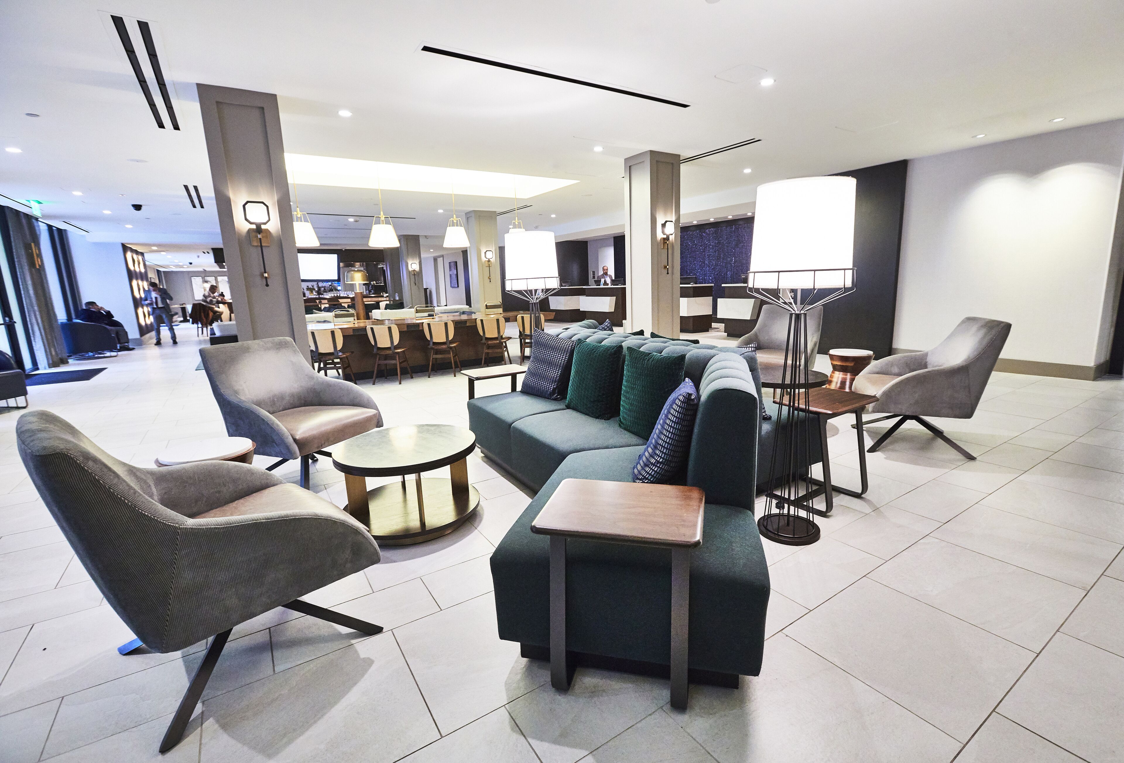 A modern hotel lobby with seating areas, a reception desk, and a dining area.