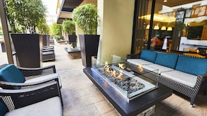 An outdoor seating area with wicker furniture, a glass-top fire pit, and potted plants.