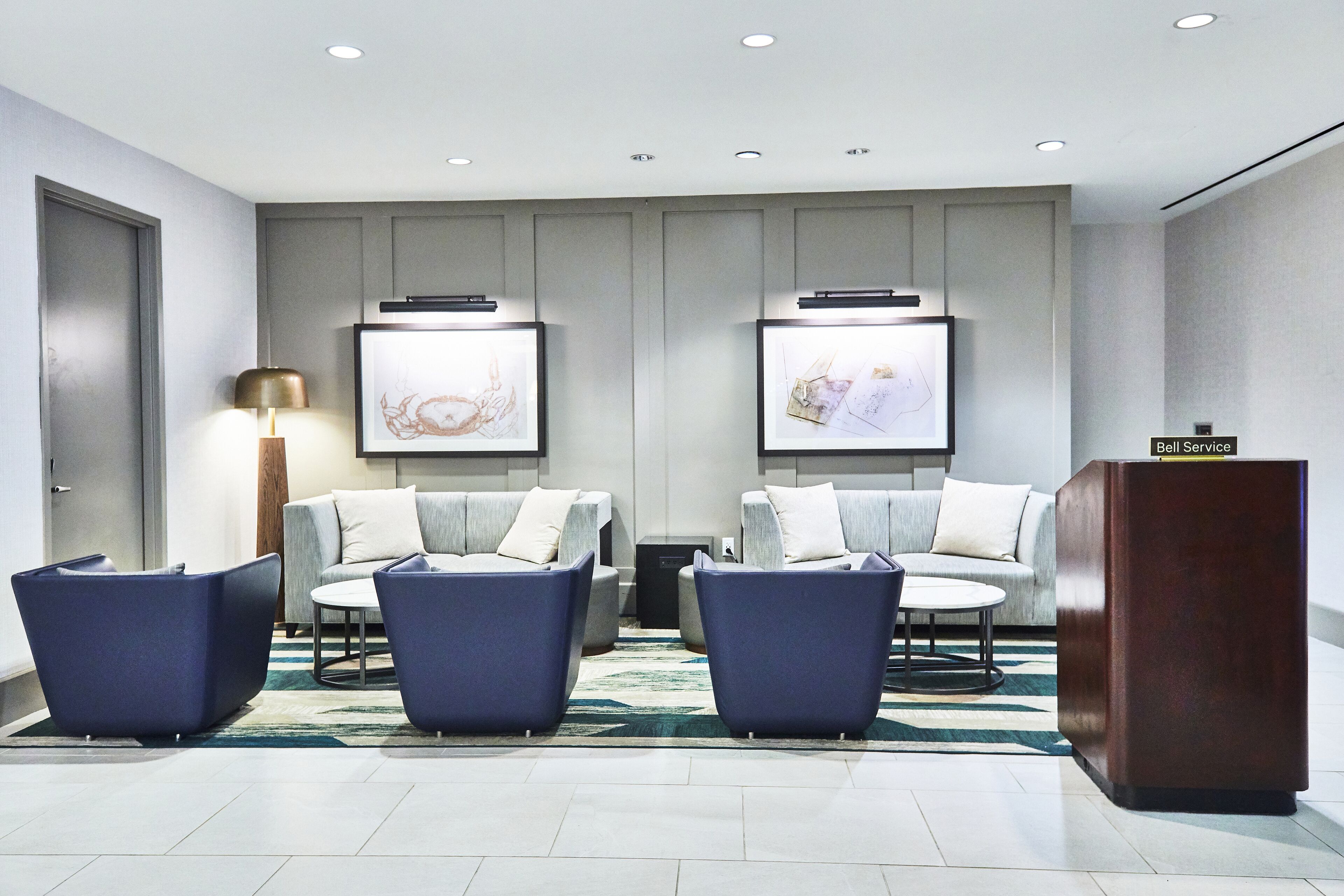 A modern lobby with two sofas, a coffee table, a lamp, and a 'Bell Service' sign.