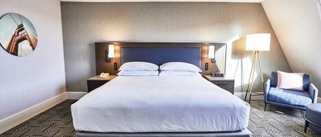 A hotel room with a large bed, a headboard, bedside tables with lamps, a chair, and a floor lamp.