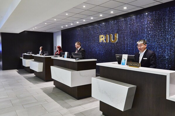 A reception area with three reception desks, each with a nameplate, and a large 'RIU' sign on the wall.