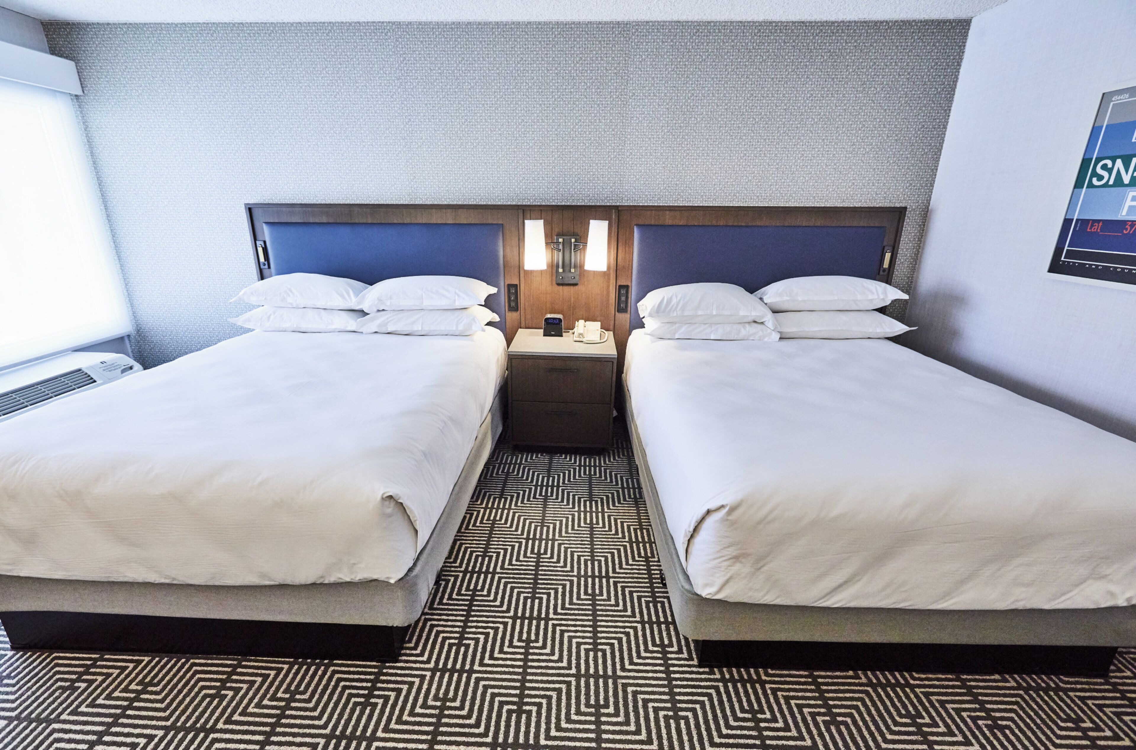 A hotel room with two beds, a patterned floor, and a wall-mounted light fixture.