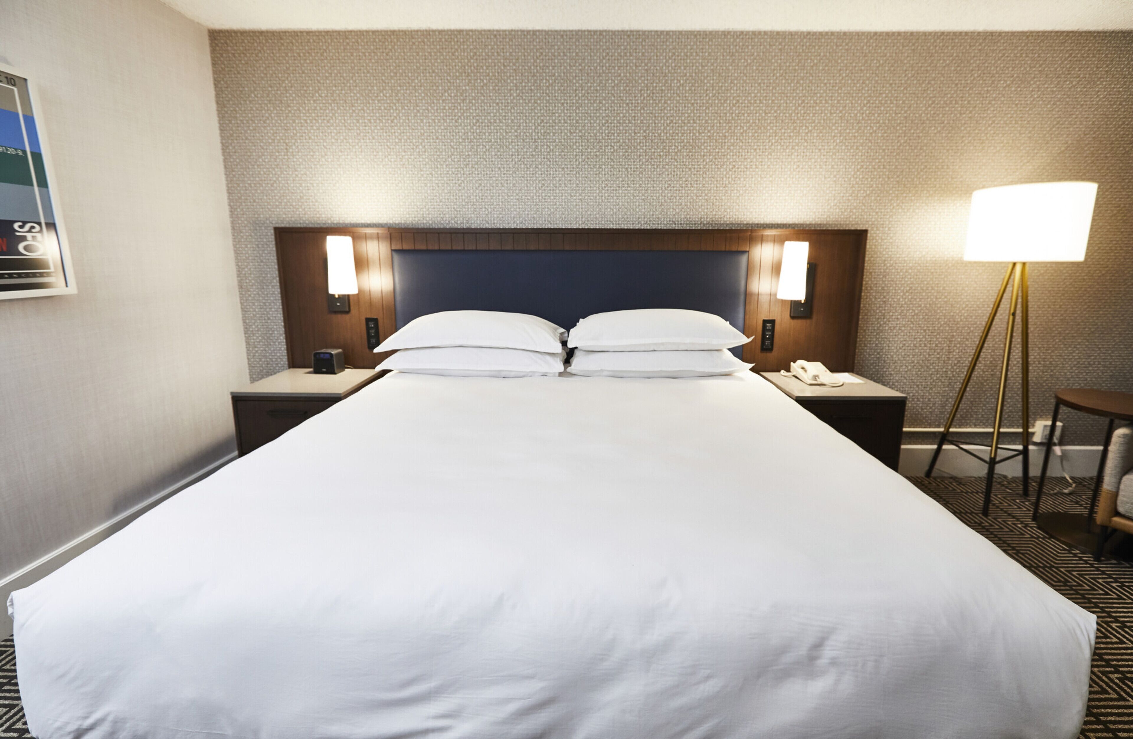 A hotel room with a large bed, two bedside tables with lamps, a small table with a chair, and a wall-mounted TV.