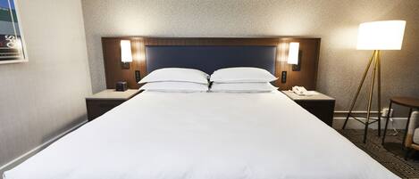 Et hotelværelse med en stor seng, to sengeborde med lamper, et lille bord med en stol og et TV ophængt på væggen.