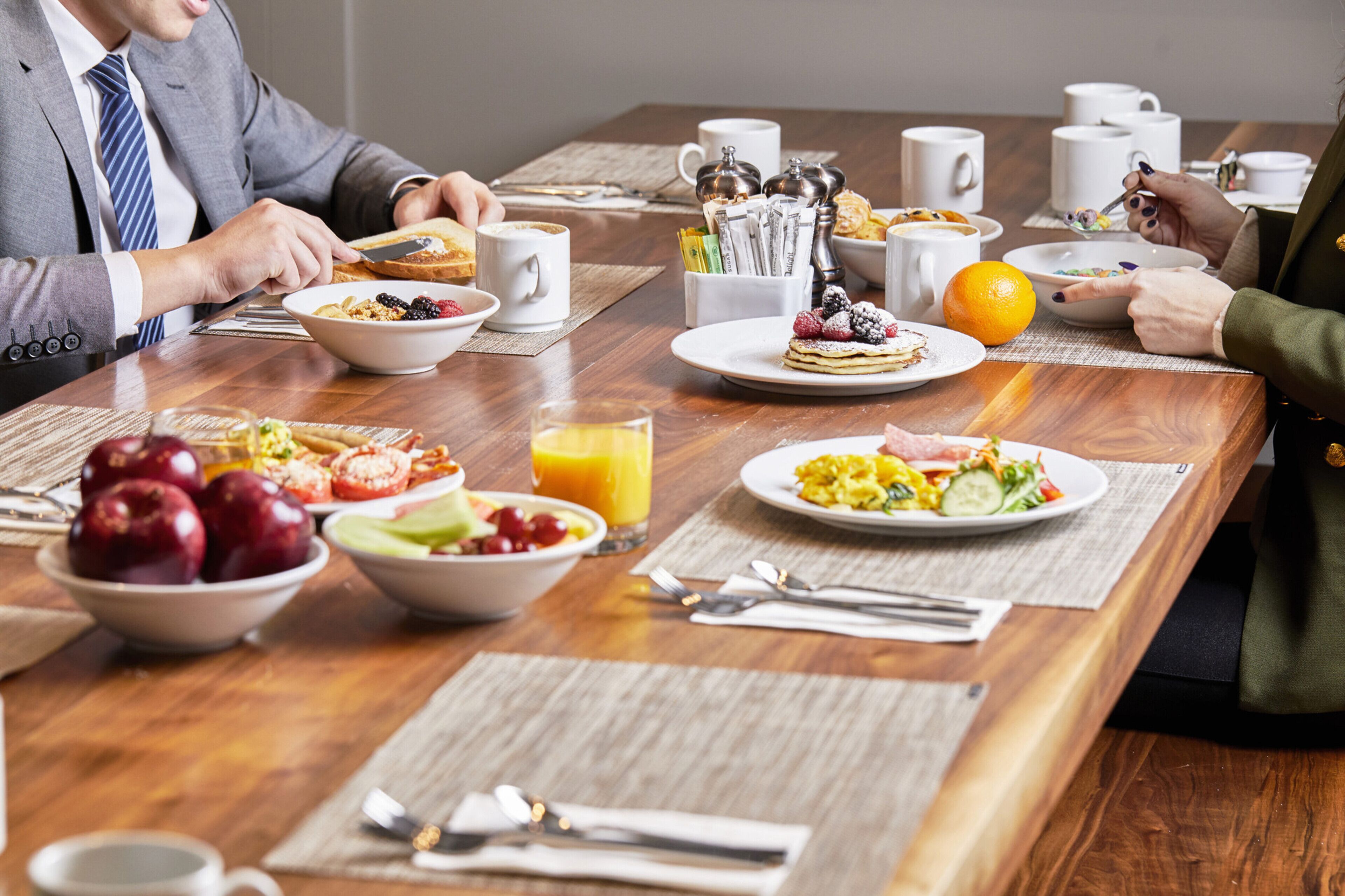 A breakfast setting with various dishes, including fruits, cereal, and pastries, on a wooden table.