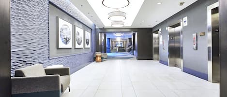 A modern hotel lobby with a long corridor, seating area, and elevators.