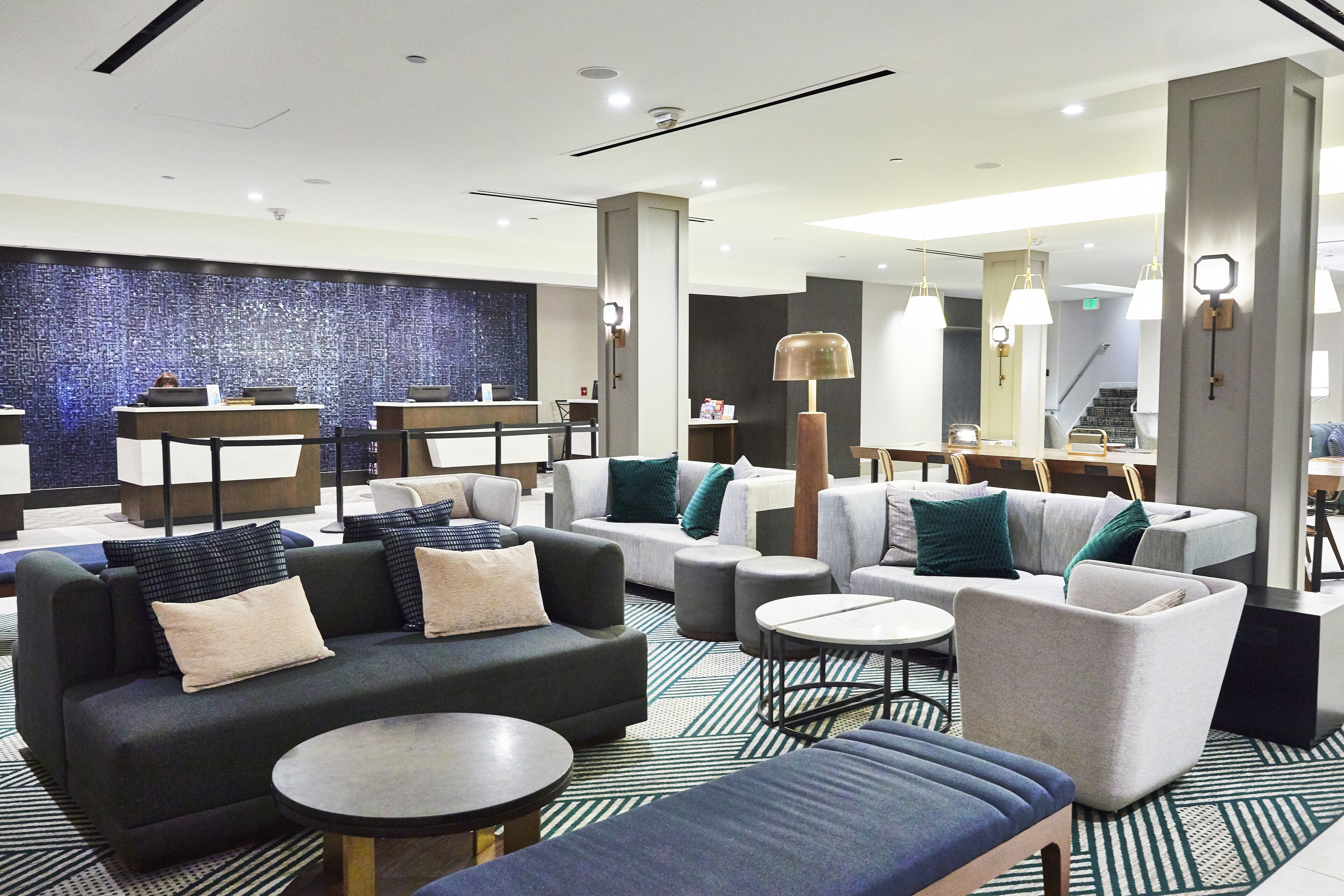 A modern hotel lobby with sofas, armchairs, and a reception desk.