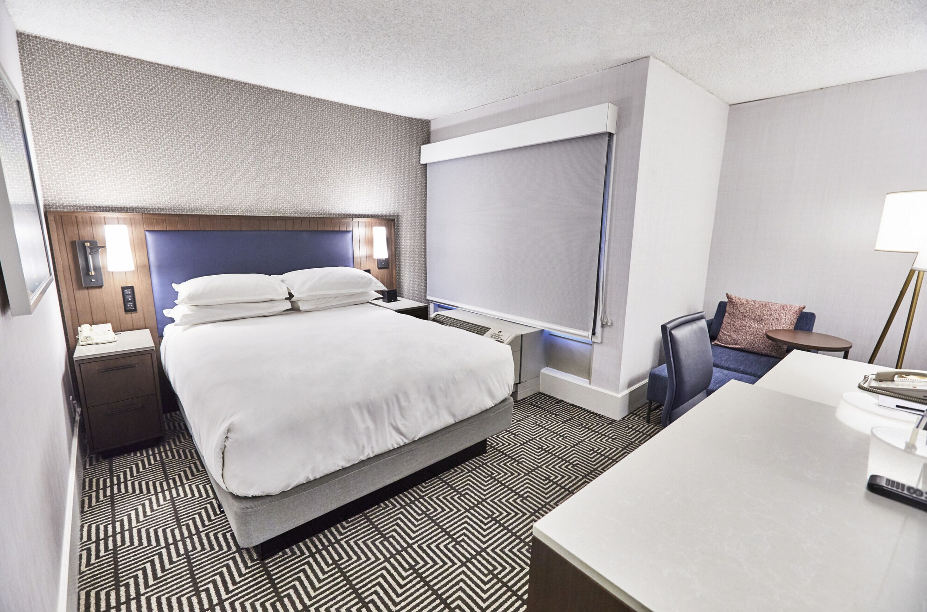 A hotel room with a large bed, a desk, a chair, and a small table.