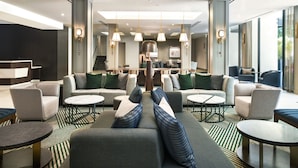 A modern hotel lobby with a central seating area, a reception desk, and a staircase leading to upper floors.