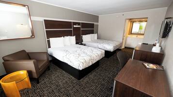 Quarto de hotel com duas camas, uma escrivaninha, uma cadeira e um sofá pequeno.