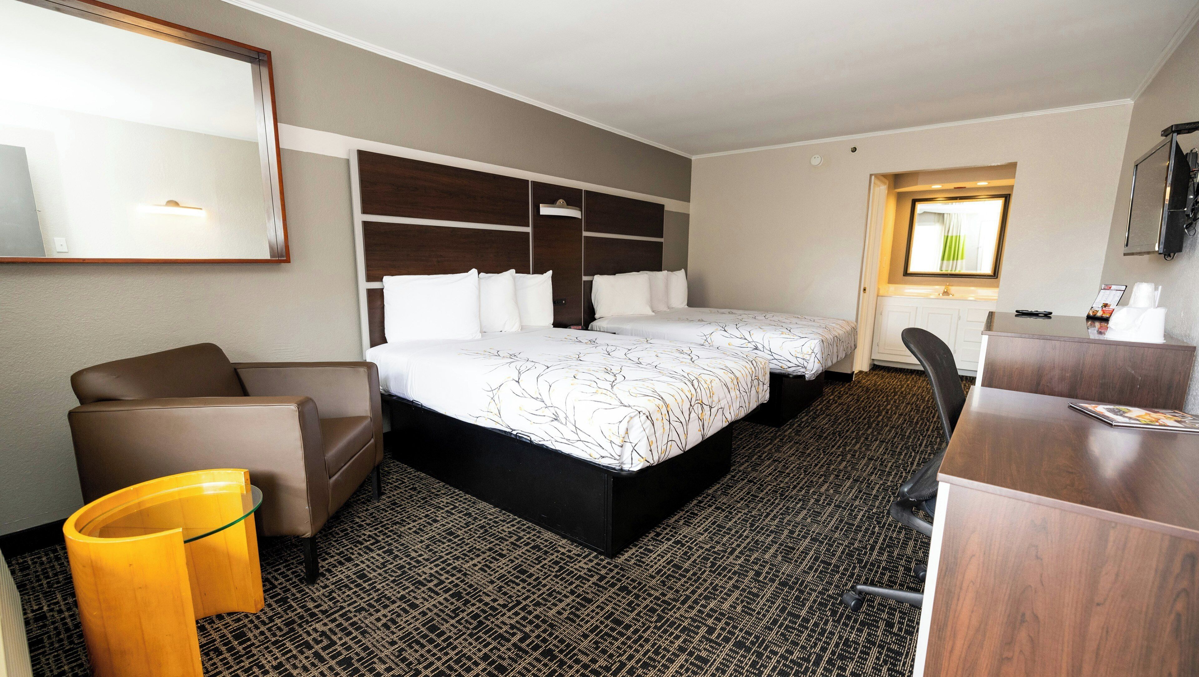 A hotel room with a bed, a desk, a chair, a small table, and a mirror.
