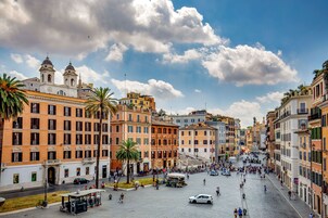 A historic square with classical architecture, a central fountain, and palm trees.