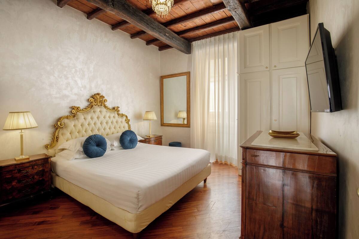 A bedroom with a large bed, wooden headboard, bedside lamps, a dresser, a mirror, and a television.