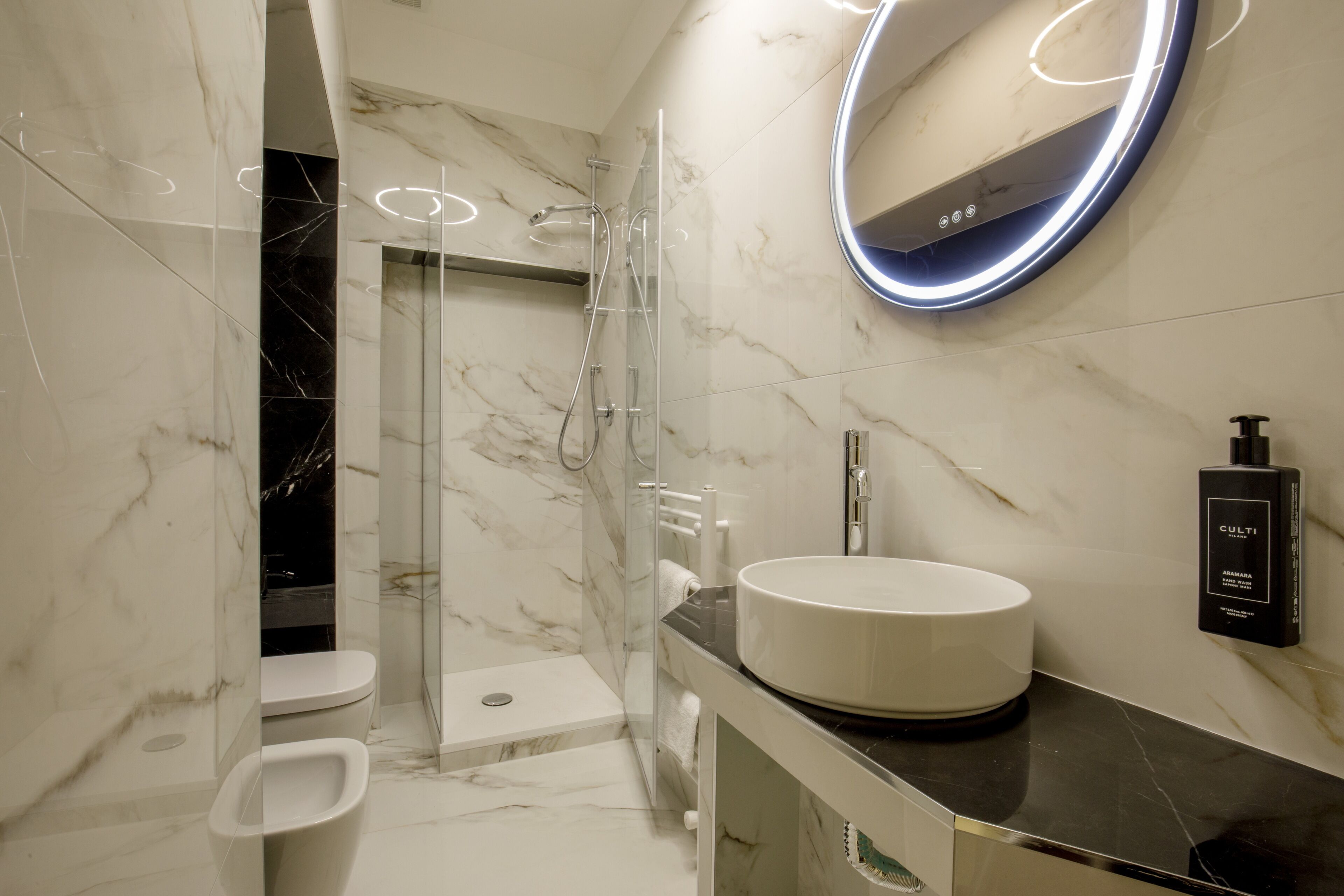 A modern bathroom with a glass-enclosed shower, a white sink, and a marble-tiled wall.