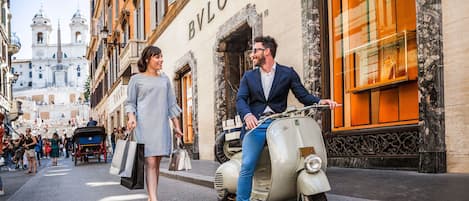 A vintage Vespa parked in front of a boutique store with a classic European architectural style.