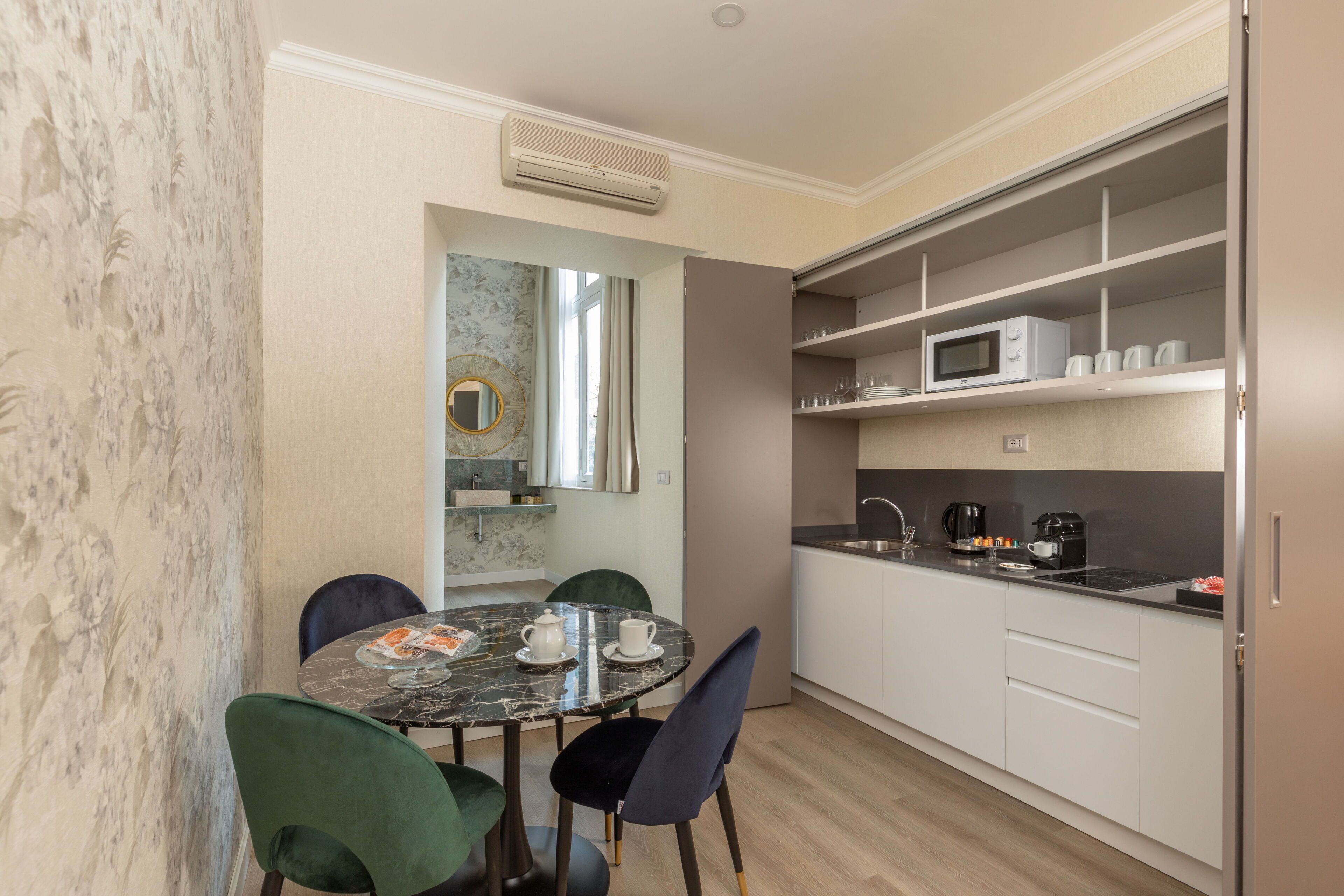 A compact kitchen with white cabinets, a microwave, and a coffee maker. There is a dining table with chairs and a small island with a marble top.