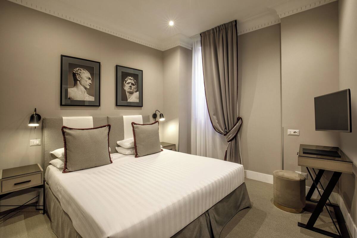 A modern hotel room with a large bed, two bedside tables, a flat-screen TV, and framed artwork on the walls.