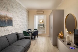 Un soggiorno moderno con un divano grigio, una zona pranzo con tavolo e sedie, una cucina con un piano di lavoro in marmo e un televisore su un mobile.