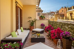 A balcony with a sofa, a glass-top table with drinks, and potted plants.