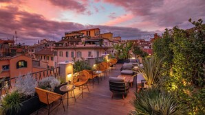 Une terrasse sur le toit, aménagée avec des meubles en osier, des plantes en pot et offrant une vue sur les bâtiments environnants.