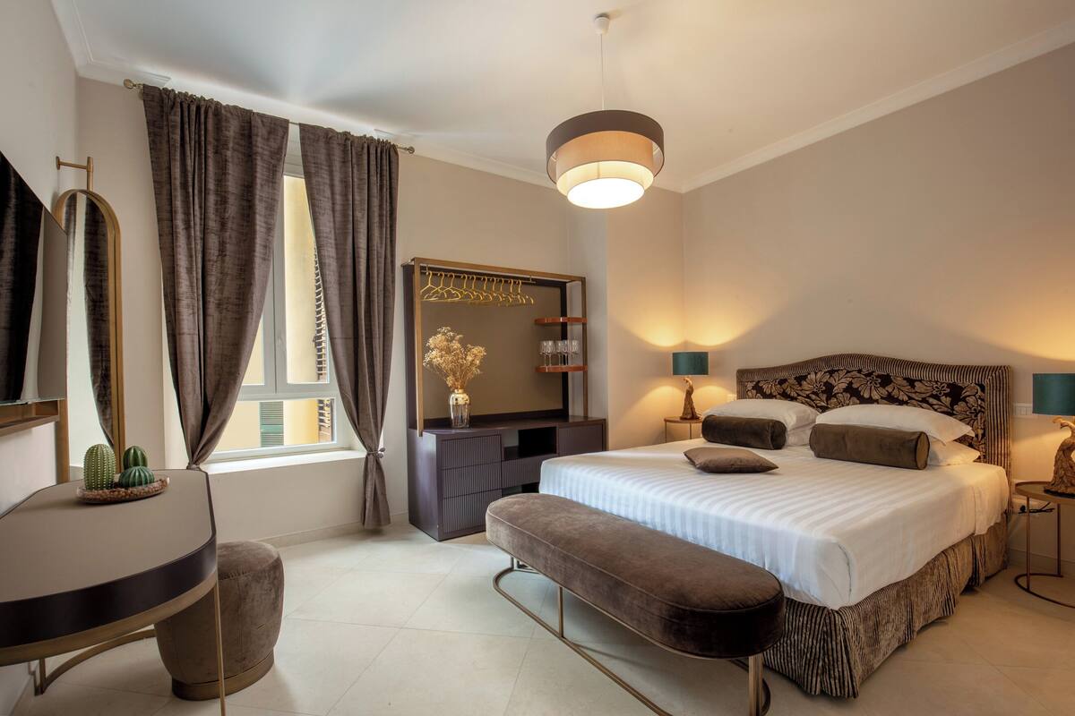 A modern bedroom with a large bed, bedside tables, a bench, a dresser, and a mirror.
