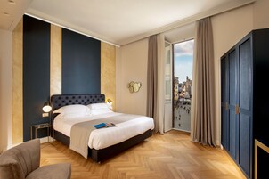 Ein modernes Hotelzimmer mit einem großen Bett, einem Nachttisch, einem Sessel und Blick auf die Stadt durch das Fenster.