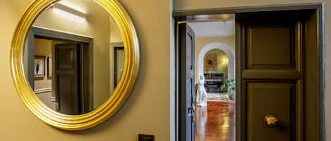 A hallway with a large mirror, a door, and a view into a room with a wooden floor and a statue.