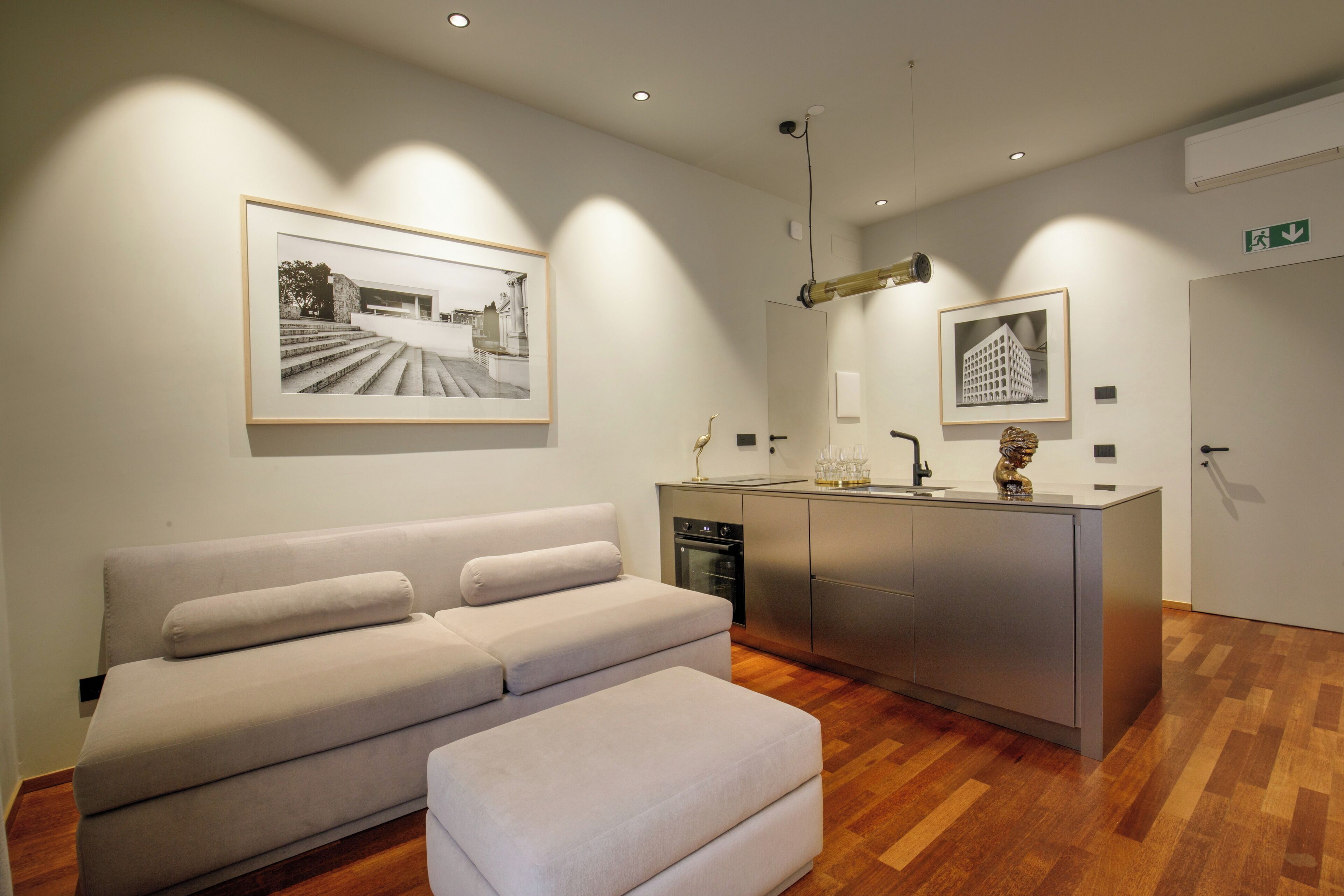 A modern hotel lobby with a neutral color scheme, a sofa, a kitchenette, and framed photographs on the walls.