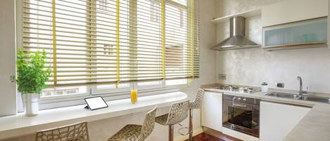 A modern kitchen with a built-in oven, a stainless steel range hood, and a window with blinds.