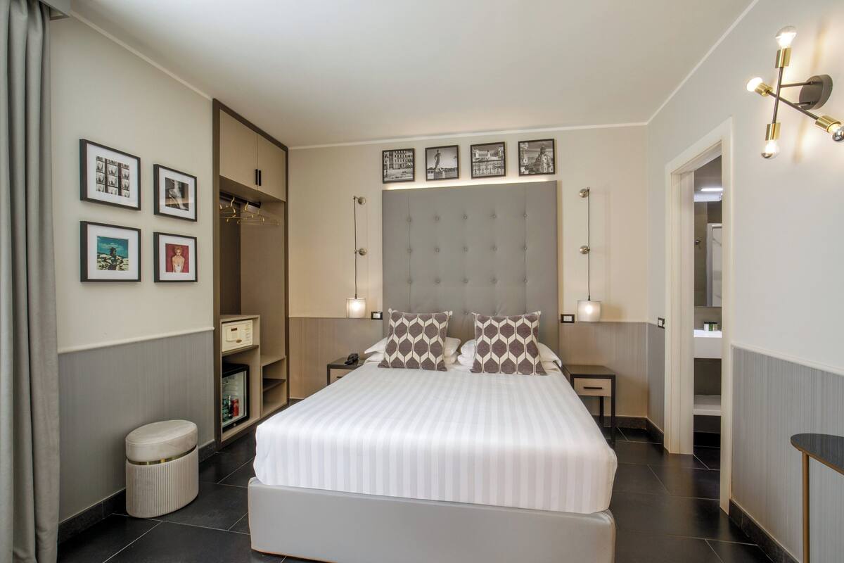 A modern hotel room with a large bed, a wardrobe, a vanity, and a small seating area.