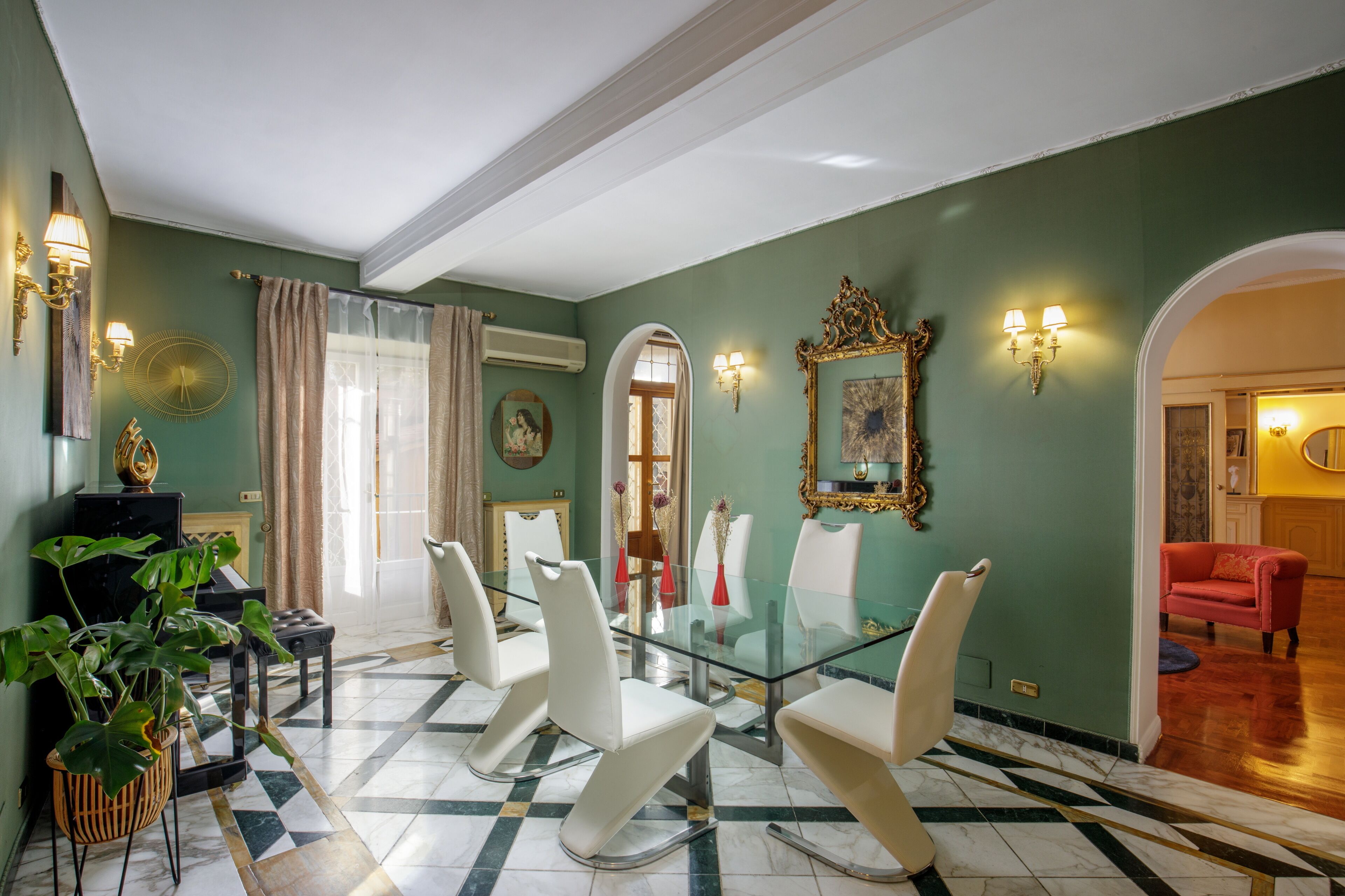 Un coin repas avec une table en verre et des chaises blanches, une plante en pot et un miroir au mur.