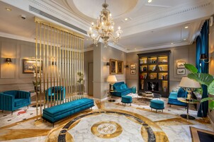 A luxurious lobby with a grand chandelier, blue sofas, and a marble floor.